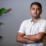 Portrait of a confident adult man with arms crossed, standing in a well-lit indoor setting.