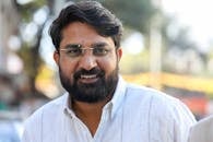Smiling man with beard and glasses in an outdoor setting, exuding warmth and friendliness.
