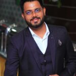 Stylish man in a dark suit smiling confidently indoors.